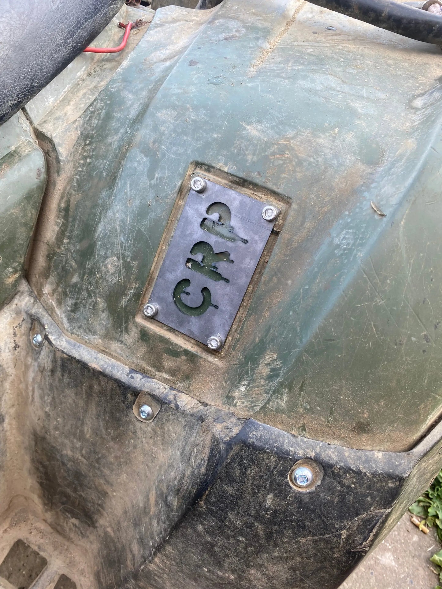 A dark gray metal honda custom 3mm fender safety plate with crp cut out mounted on a green muddy vehicle body
