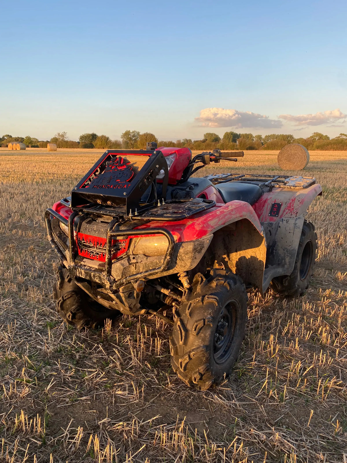 Red and black honda foreman atv with rugged mud-splattered tires and custom front rack featuring radiator relocation kit