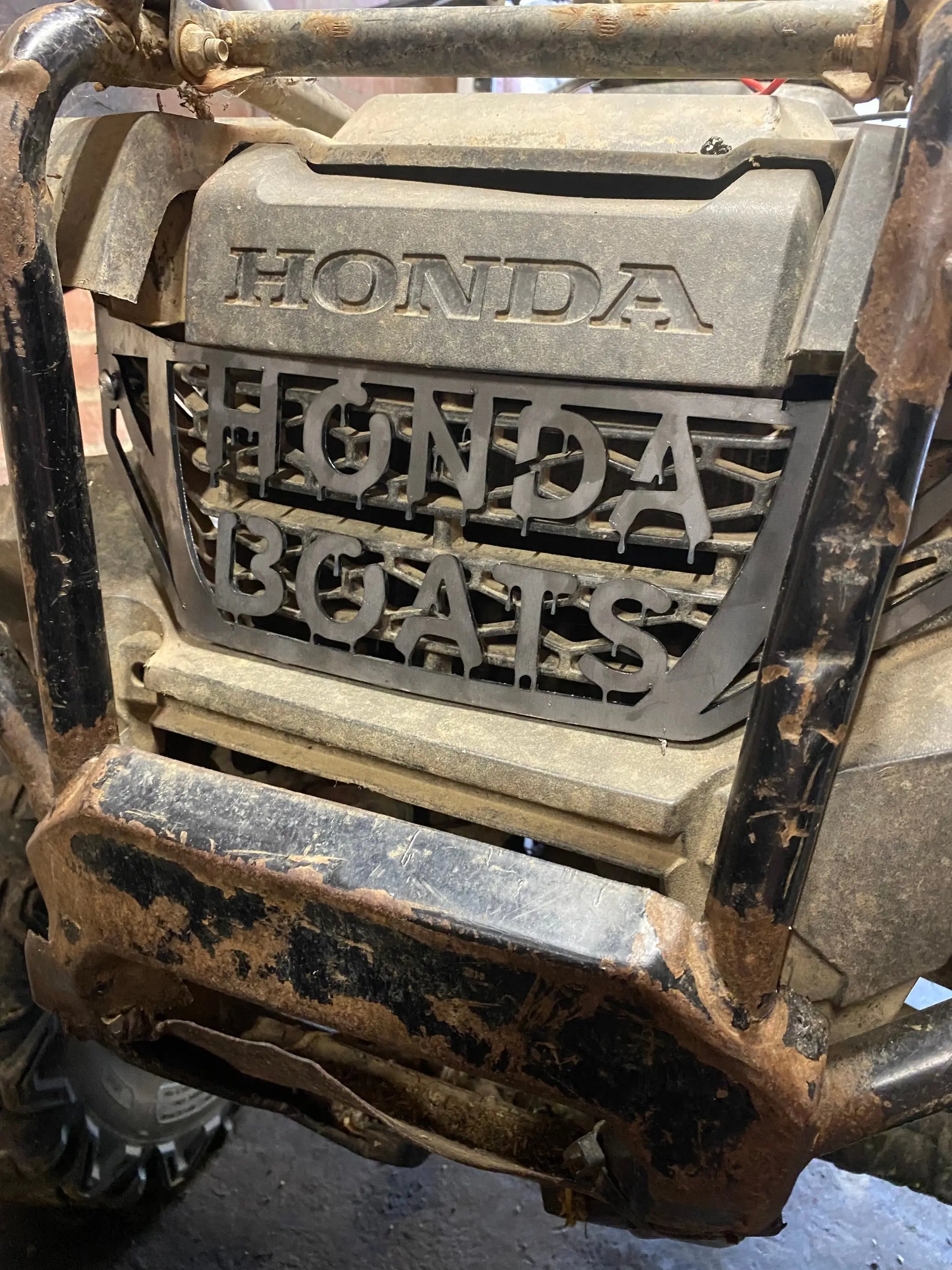 Mud-splattered black honda trx 420 2014 custom heavy-duty grille cover with embossed branding on rugged off-road front end