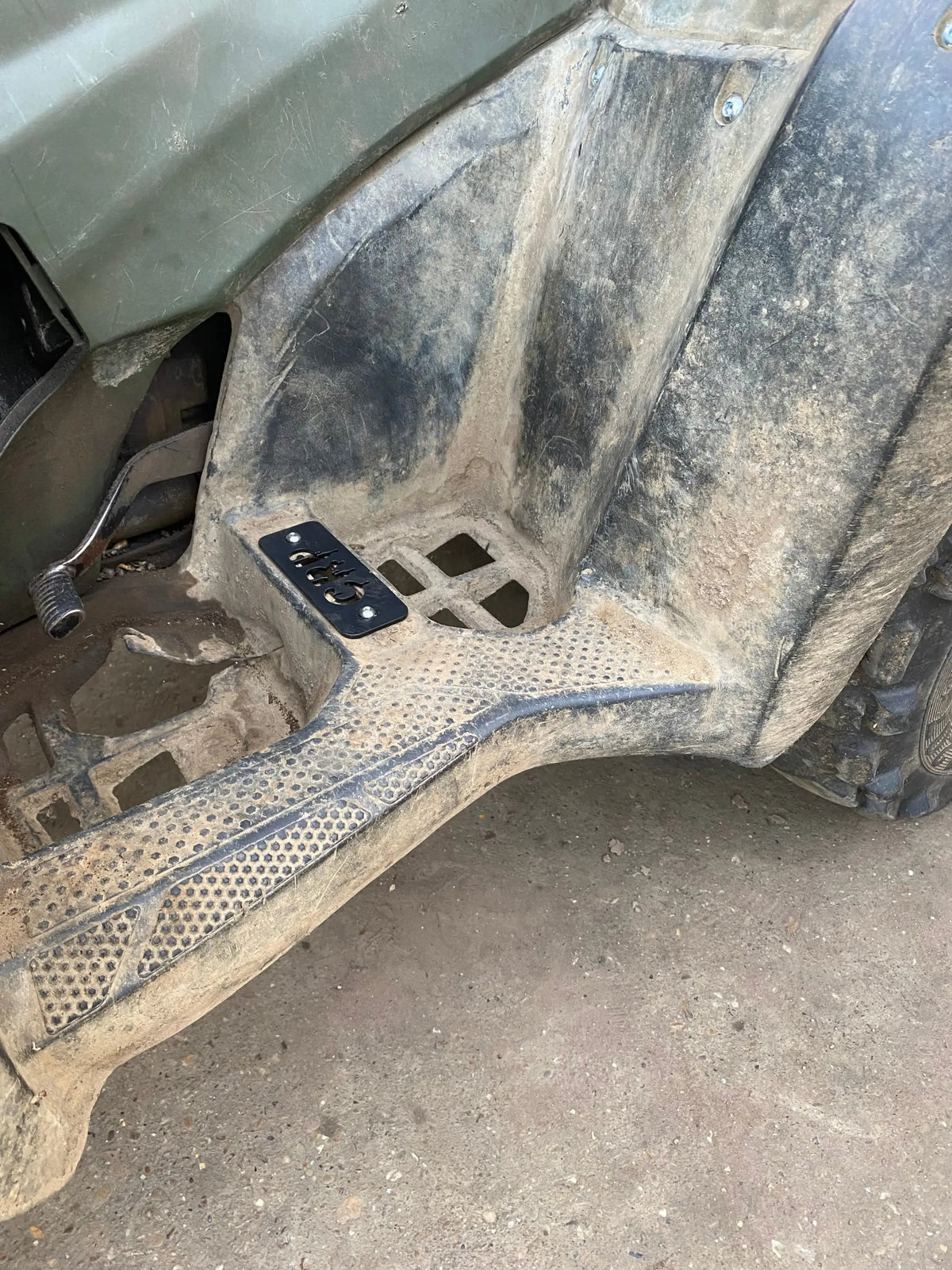 Black heavy-duty flat footpeg plate with four circular cutouts mounted in muddy footwell for honda trx 420 500 520