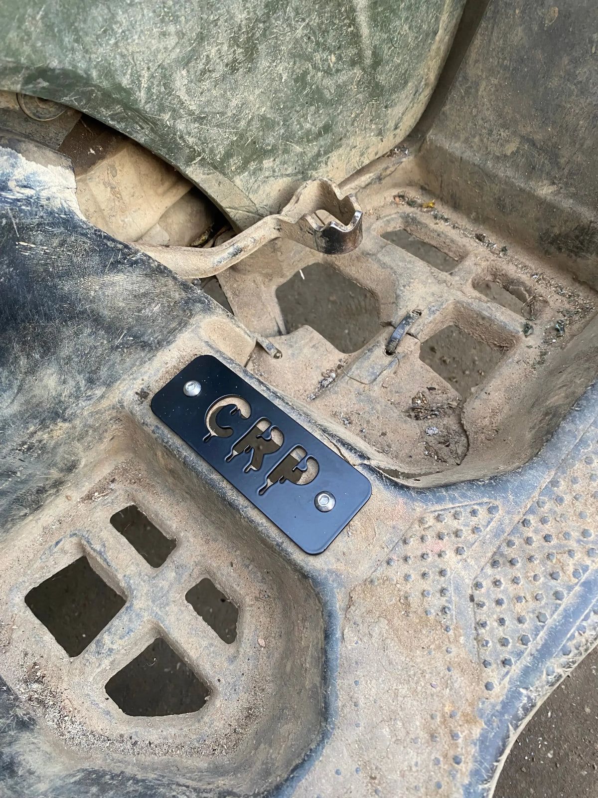 Black rectangular heavy-duty flat footpegs with cut-out crp letters mounted on muddy floor of honda trx 420 500 520