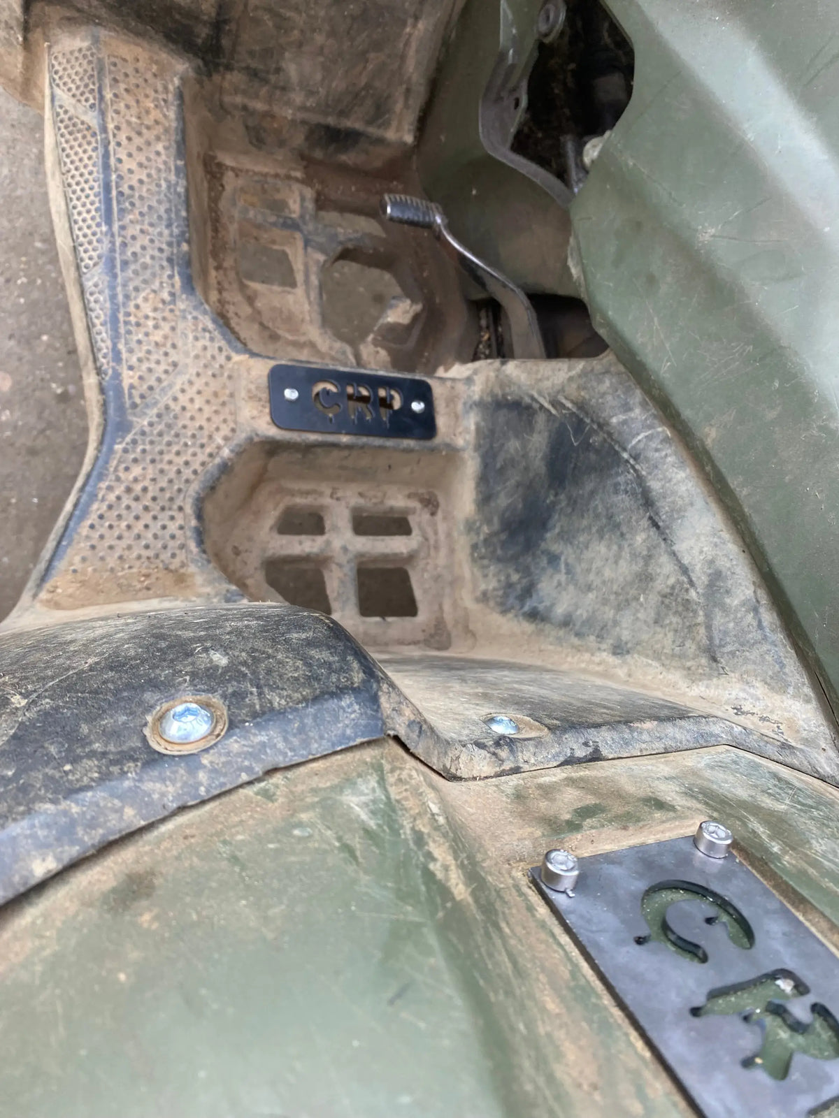 Black metal heavy-duty flat footpegs with cut-out lettering mounted on muddy green atv floor for honda trx 420 500 520